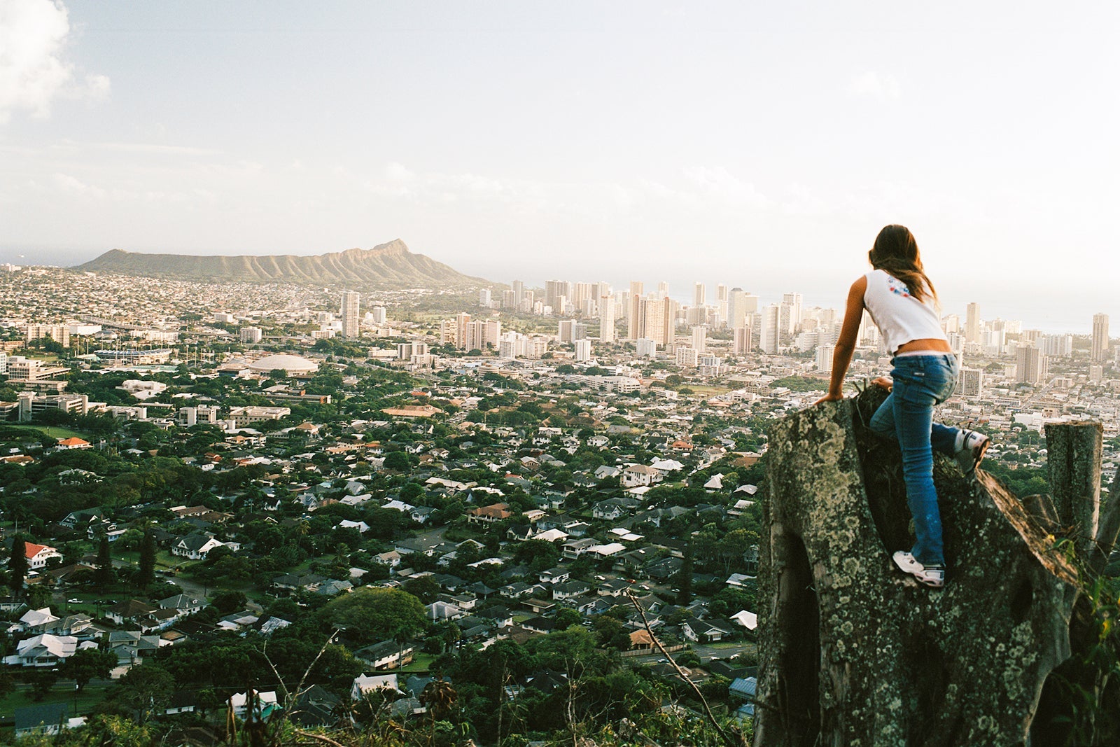 Girl (12-13) climbing stump overlooking cityscape, rear view