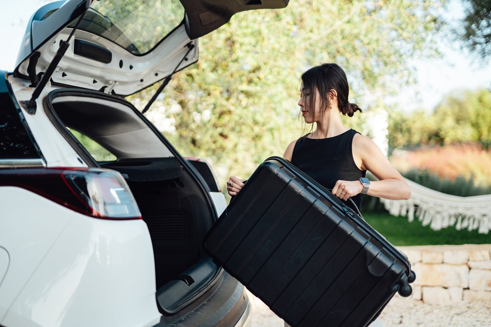Young woman loading luggage into car, getting ready for a road trip