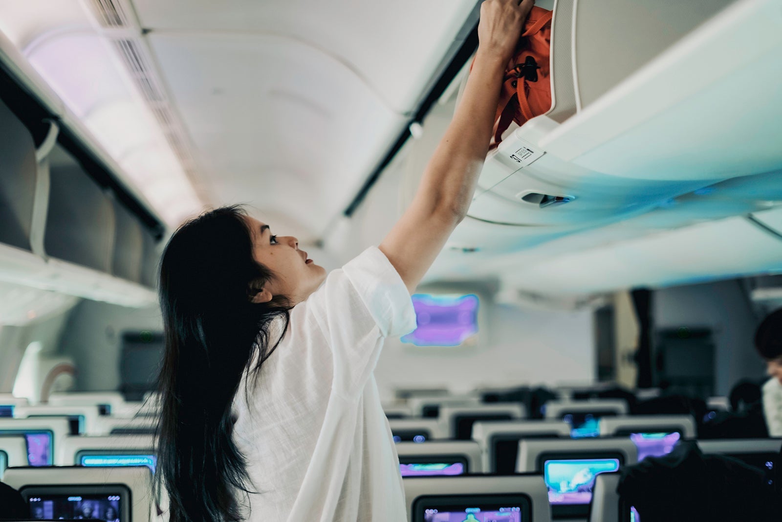 woman passenger in action of trying herself to prepare the bag luggages equips to storage on overhead locker compartment of the airplane, support or help require for woman traveler alone