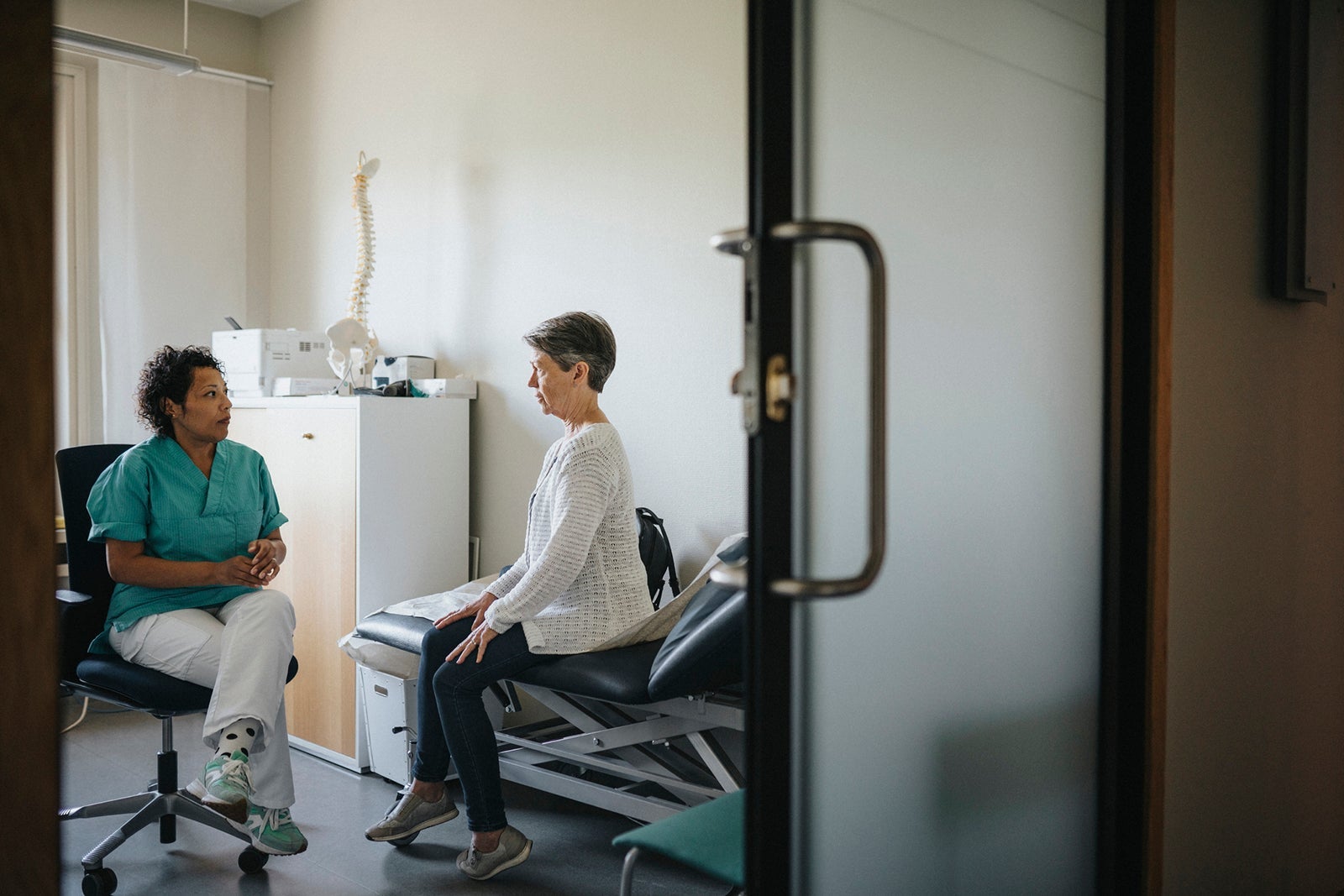 Doctor discussing with female patient seen through doorway in clinic