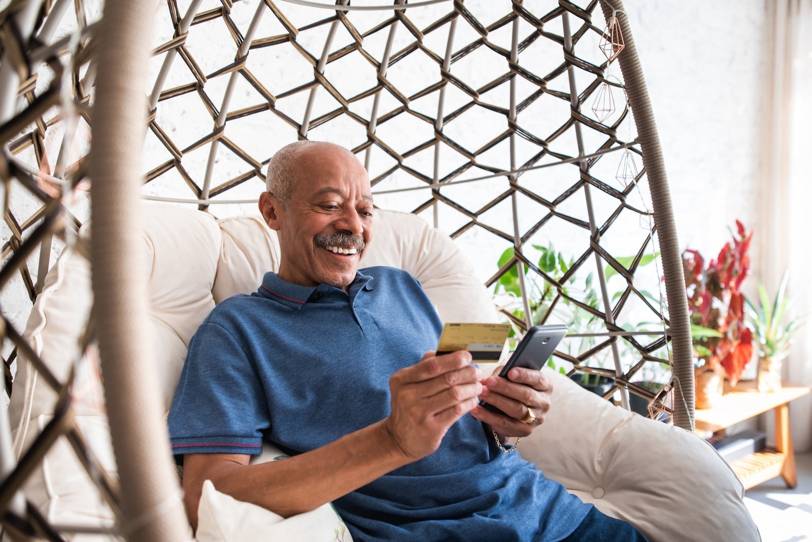 adult senior man using mobile phone and holding credit card in hand in the living room at home