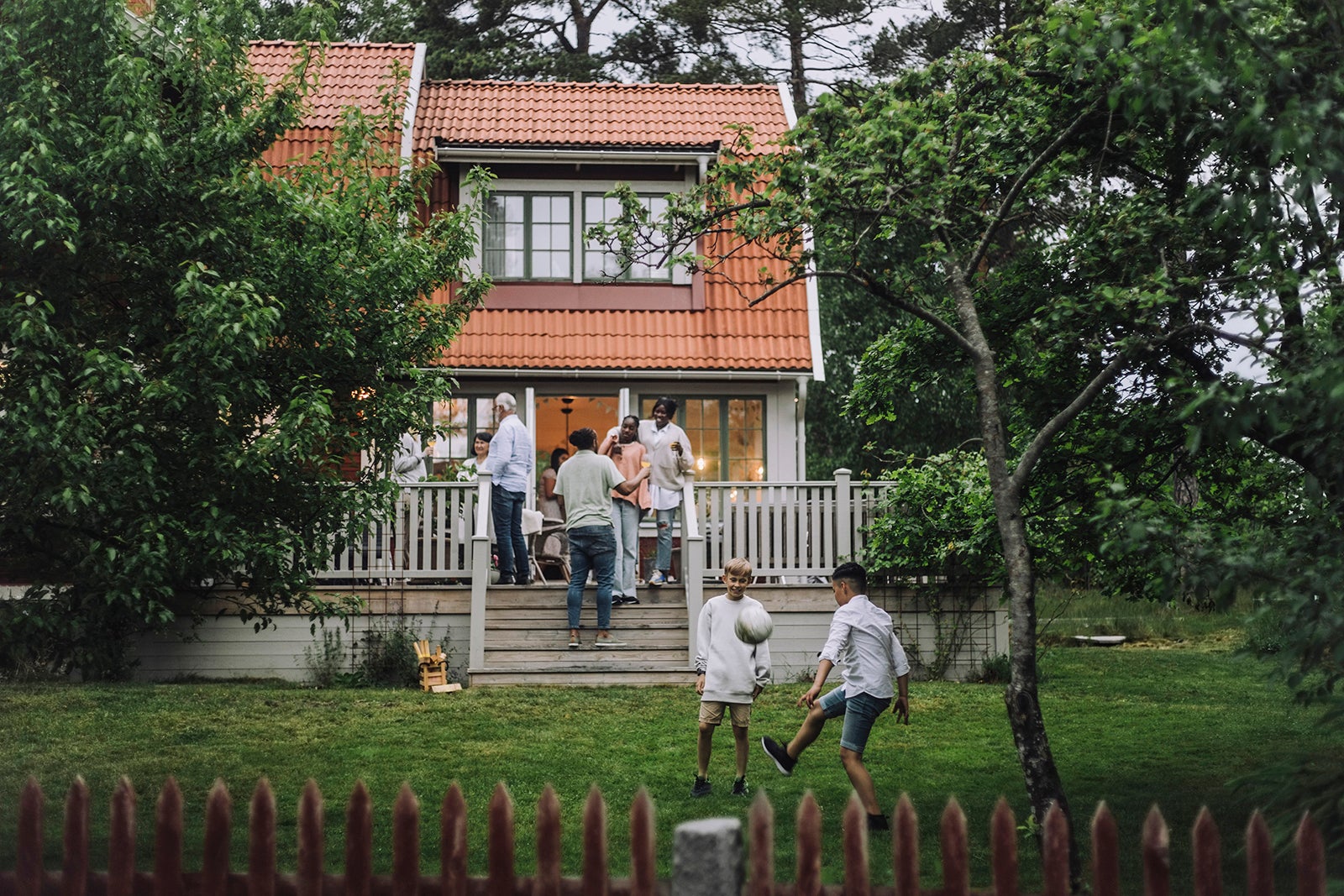Boys playing soccer in back yard while family enjoying party on porch