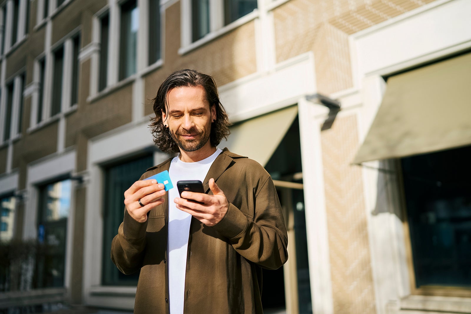 man using smart phone doing online shopping through credit card on sunny day